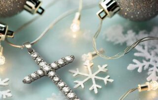A diamond cross pendant on a frosted glass surface 1 surrounded by delicate snowflakes glowing fairy lights and silver Christmas ornaments