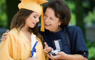 Graduation jewelry gift exchange between grandmother and granddaughter in cap and gown, celebrating academic achievement.