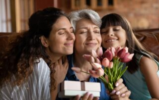 Grandmother receiving a jewelry gift and flowers from her daughter and granddaughter for International Women’s Day.