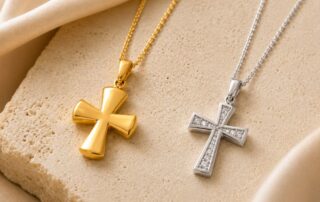 White gold and yellow gold cross necklaces displayed on a luxury neutral stone background, comparing classic and modern gold cross styles.